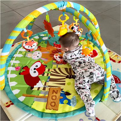  bébé sur le ventre sur un tapis d’éveil à motifs d’animaux avec arches multicolores et jouets suspendus