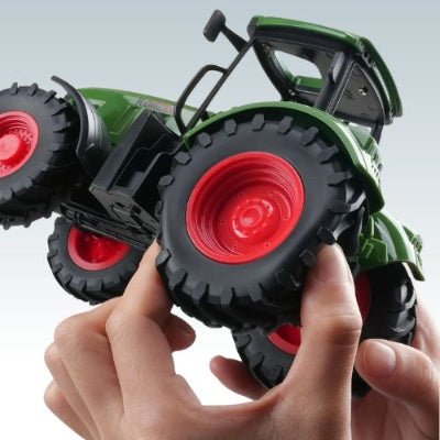 gros plan des roues rouges et des pneus noirs du tracteur jouet vert tenu dans les mains